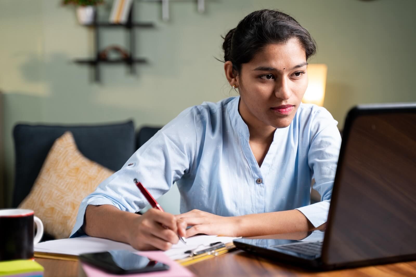 person taking notes in front of laptop